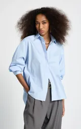Camisa de corte oversize color celeste, con cuello clásico, cierre frontal de botones y mangas largas con puños abotonados.