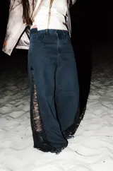 Jean de denim negro de corte wide leg, con paneles laterales de encaje negro mate a lo largo de las piernas.