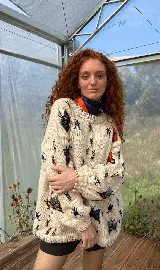 Buzo tejido de punto color crudo, con diseño oversized y cuello redondo. Presenta un bordado artesanal de insectos y mariposas en diversos colores distribuidos por toda la prenda. Cuenta con puños y ruedo acanalados con detalles de costuras en contraste.