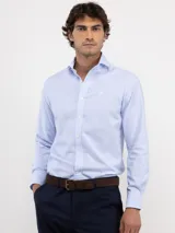 Camisa de manga larga con diseño de rayas verticales finas en color celeste y blanco. Presenta cuello clásico, cierre frontal con botones y logo bordado en el pecho.