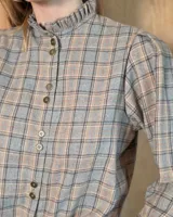 Camisa de algodón con estampado de rayas verticales finas, cuello alto con volados, cierre frontal con botones dobles y mangas largas con puños elásticos terminados en volados.