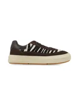 Sneaker de diseño urbano con combinación de cuero marrón y paneles de pelo con estampado animal print tipo cebra. Cuenta con suela de plataforma en tono crema y cordones al tono.