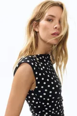 Vestido midi entallado de punto elástico en color negro con estampado de lunares blancos. Presenta escote bote, mangas japonesas y laterales fruncidos que realzan la silueta.