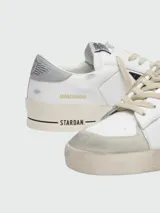 Championes Golden Goose modelo Stardan, color blanco con estrella negra de cuero texturizado en el lateral, detalles en gris y suela color crema con efecto desgastado.