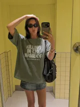 Remera gris con efecto acid wash y diseño oversize. Presenta un estampado frontal con la inscripción "KILLING IN THE NAME OF" y la frase "NOW YOU DO WHAT THEY TOLD YA".