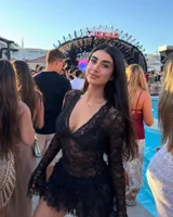 Vestido corto negro de encaje transparente, con escote en V profundo, mangas largas acampanadas y falda con volados. Incluye short interior.
