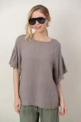 Blusa de lino color marrón topo, de corte holgado, con escote redondo y mangas cortas amplias adornadas con detalles de encaje y volados.