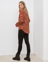 Blusa de manga larga color marrón terracota con estampado floral en tonos rojos, blancos y verdes. Presenta un escote en V con cuello mao y mangas que se pueden ajustar con presilla y botón.