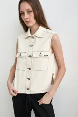 Chaleco de denim crudo de corte recto, con cuello camisero, sin mangas y cierre frontal con botones metálicos. Cuenta con dos bolsillos delanteros con solapa y costuras pespunteadas en contraste.