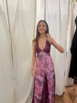 Vestido largo sin mangas con escote en V halter y aberturas laterales (cut-outs) en la cintura. El cuerpo superior presenta un llamativo diseño estampado multicolor, mientras que la falda larga es de tejido texturizado brillante en color verde esmeralda con inserciones godet en el ruedo.