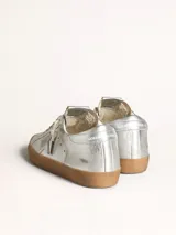 Zapatilla Golden Goose modelo Super-Star color plateado con estrella lateral y suela marrón.