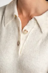 Sweater de tejido de punto color blanco roto o crema, con textura jaspeada. Presenta cuello polo y un escote con tres botones nacarados. El calce es holgado (oversize) y tiene mangas largas.