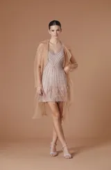 Trench ligero de tul color nude, con diseño abierto, solapas clásicas y mangas largas. Presenta una caída fluida y transparente, ideal para superposiciones elegantes.