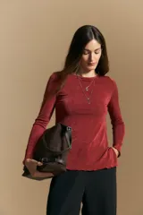 Top de manga larga con textura suave y leve brillo. Presenta una silueta al cuerpo, tajos laterales y terminaciones onduladas en el ruedo.