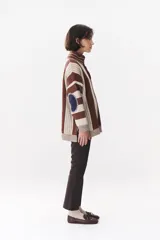 Buzo de punto con diseño de rayas verticales en tonos verde y azul marino. Presenta cuello alto con cierre frontal, hombros caídos y coderas en contraste de color marrón con costuras decorativas visibles.