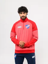Buzo deportivo de medio cierre marca Umbro del Club Nacional de Football. Presenta un diseño en tonos azul y gris jaspeado, con cuello alto, mangas largas y detalles de costuras en contraste. Incluye el escudo del club y logo de la marca en el pecho.