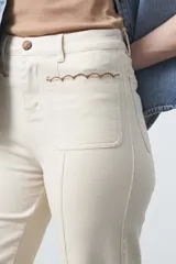 Pantalón de fit recto color beige, confeccionado en cotton spandex. Presenta costuras visibles y bordados decorativos en tono dorado/marrón claro. El ruedo del pantalón tiene un borde festoneado.