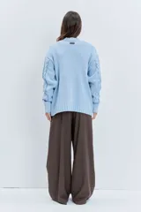 Sweater de punto color celeste, con diseño de trenzas y detalles de cordones entrelazados en el frente y las mangas. Presenta cuello redondo y puños acanalados.