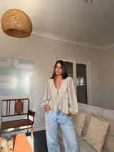 Camisa de tela liviana color celeste, con escote en V, mangas largas abullonadas con puños elásticos y detalle de volado fruncido en el frente con cierre de cordones ajustables.