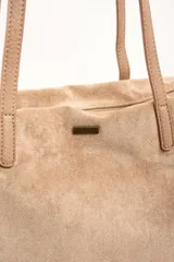 Bolso tipo shopper de gamuza vegana color tostado, con doble asa larga para hombro y cierre superior. Cuenta con una pequeña placa metálica con el logo de la marca en la parte frontal.
