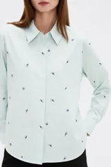 Blusa de corte holgado con cuello camisero y cierre frontal de botones. Presenta un diseño de rayas verticales finas en color azul y blanco, decorado con pequeños bordados dispersos.