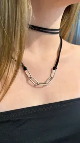 Gargantilla tipo choker compuesta por una tira de gamuza negra que rodea el cuello y una sección frontal de eslabones metálicos plateados.