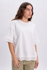 Remera manga corta de color blanco con detalles de encaje en el borde de las mangas y el ruedo, de corte holgado y diseño casual.