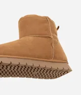 Bota de caña media color marrón, confeccionada en poliéster con acabado suave. Cuenta con interior forrado en piel sintética para mayor abrigo, tirador trasero y suela plana de goma con diseño dentado.