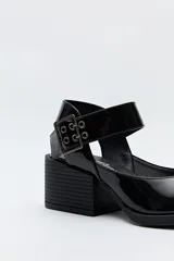 Zapato negro tipo zueco con acabado charol, tira ancha con hebilla metálica y taco ancho de altura media.