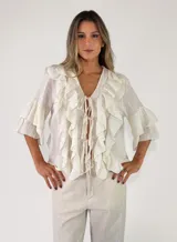 Blusa blanca de manga corta abullonada con volados en cascada y cierre delantero con cordones para atar.