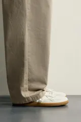 Zapatillas deportivas barefoot de hombre elaboradas en piel. Diseño en color blanco con detalles en negro y beige en el talón, y suela plana de goma marrón.