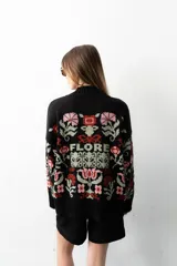 Buzo tejido de algodón negro con diseño jacquard de flores multicolor, cuello en V y mangas largas.