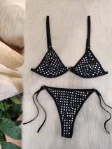 Conjunto de bikini negro con apliques de tachas cuadradas plateadas. El corpiño es de estilo triangular con una argolla central metálica y breteles regulables. La bombacha es de corte colaless con tiras laterales ajustables y argollas metálicas en los extremos.