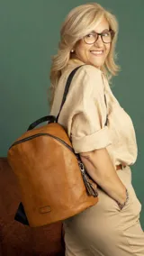 Mochila de tamaño mediano confeccionada en símil cuero color suela, con cierre principal de gran capacidad, asa de mano superior y correas regulables. Incluye bolsillo oculto en la parte trasera y detalles metálicos.