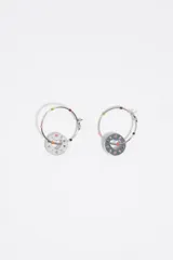 Caravanas de metal plateado con aros argolla adornados con pequeños detalles esmaltados de colores y un dije colgante circular con un corazón recortado en el centro y letras esmaltadas alrededor.