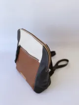 Mochila de cuero tricolor en tonos marrón tostado, negro y blanco, con bolsillo frontal con cierre, tiradores de cuero y detalle de etiqueta con logo grabado.