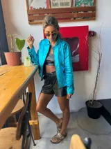 Campera turquesa de tela brillante con flecos en mangas y ruedo.