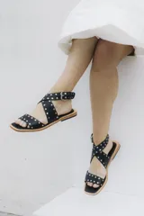 Sandalias bajas de cuero negro con tachas plateadas, tiras cruzadas y hebilla al tobillo.