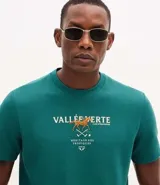 Remera masculina de manga corta color verde oscuro, con cuello redondo y corte recto. Presenta un estampado frontal con la frase "Vallée Verte" y un diseño de caballo de polo con raquetas cruzadas.