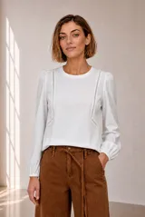 Remera blanca de manga larga con detalles de encaje en el frente y puños elásticos.