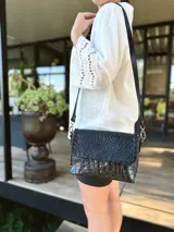 Cartera bandolera de cuero negro con textura tipo cocodrilo, correa larga regulable y forro interno de tela.