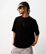 Remera oversize de tejido tipo gamuza sintética negra, con cuello redondo, manga corta y bordado de cruz gótica en el pecho.