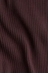 Pantalón de tiro alto, color marrón oscuro, confeccionado en tejido de punto acanalado. Presenta elástico oculto en la cintura y bajos acampanados con abertura lateral.