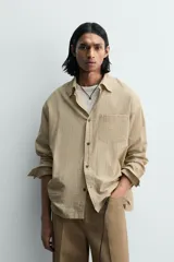 Camisa de hombre de manga larga, color beige con micro-estampado a cuadros en tonos marrones. Presenta cuello solapa abotonado (button-down), un bolsillo de parche en el pecho y cierre frontal de botonadura.