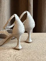 Zapato de tacón con punta fina, confeccionado en tela con aplicación de strass en la capellada y detalles en cuero en el talón, taco y pulsera. Cuenta con cierre de hebilla al tobillo y taco de altura media.