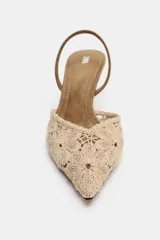 Zapato de tacón medio fino y destalonado, color beige con cuerpo de tejido bordado con motivos florales, punta fina y tira trasera elástica.