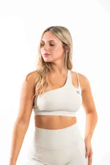 Top deportivo color crema, de un solo hombro, con logo pequeño en el frente.