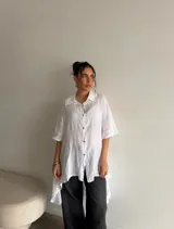 Camisola de lino color beige, de corte amplio, con cierre frontal de botones y diseño asimétrico más largo en la parte trasera.