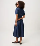 Vestido midi de jean azul, de manga corta, con bolsillos frontales con solapa, cierre frontal de botones y cinturón ajustable para anudar en la cintura.