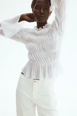 Pantalón jean de tiro alto en color blanco, con diseño de pernera recta holgada, trabillas para cinturón y cierre frontal con botón metálico. Presenta pliegues marcados al frente y bolsillos laterales.